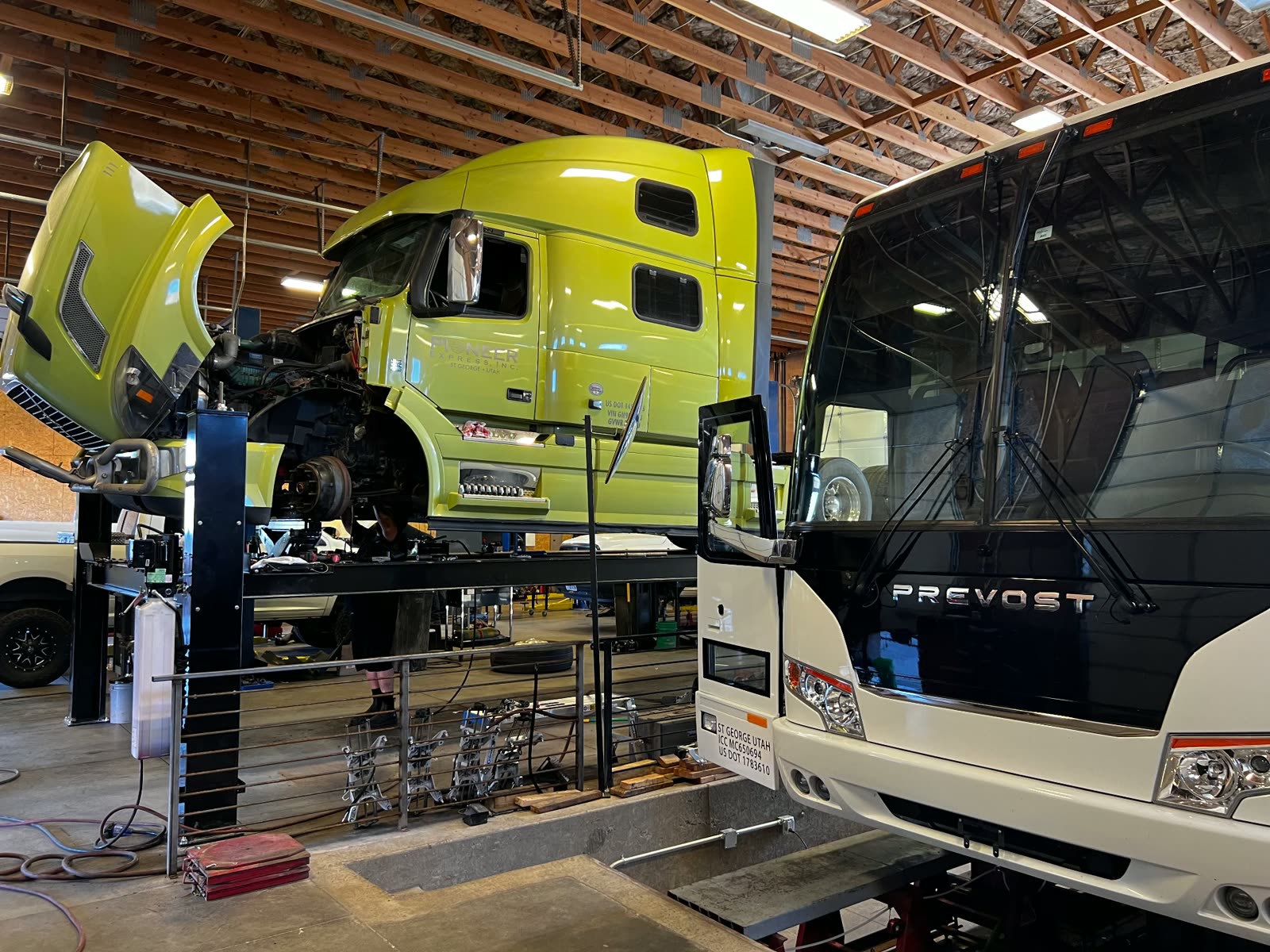 Volvo semi tractor with the hood up next to a Prevost coach in the heavy duty bay