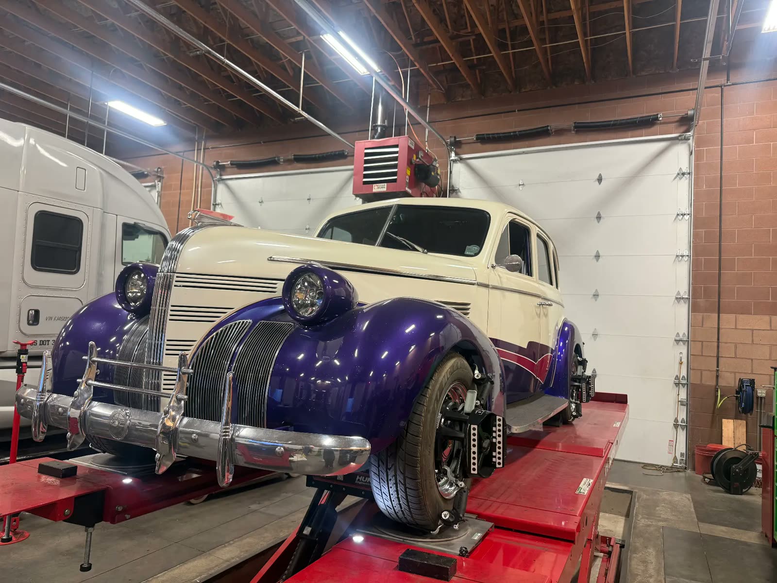 Purple and cream 1930s custom sedan being aligned next to a semi truck